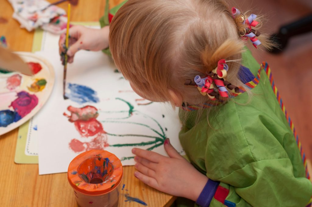 A little girl painting flowers with paintbrush. Kids creativity