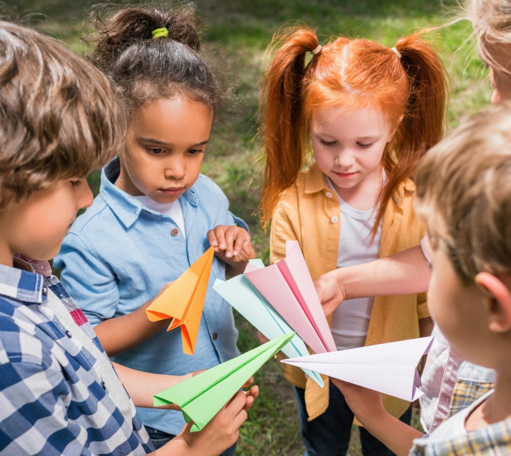 high angle view of cute multiethnic kids playing with paper planes in park