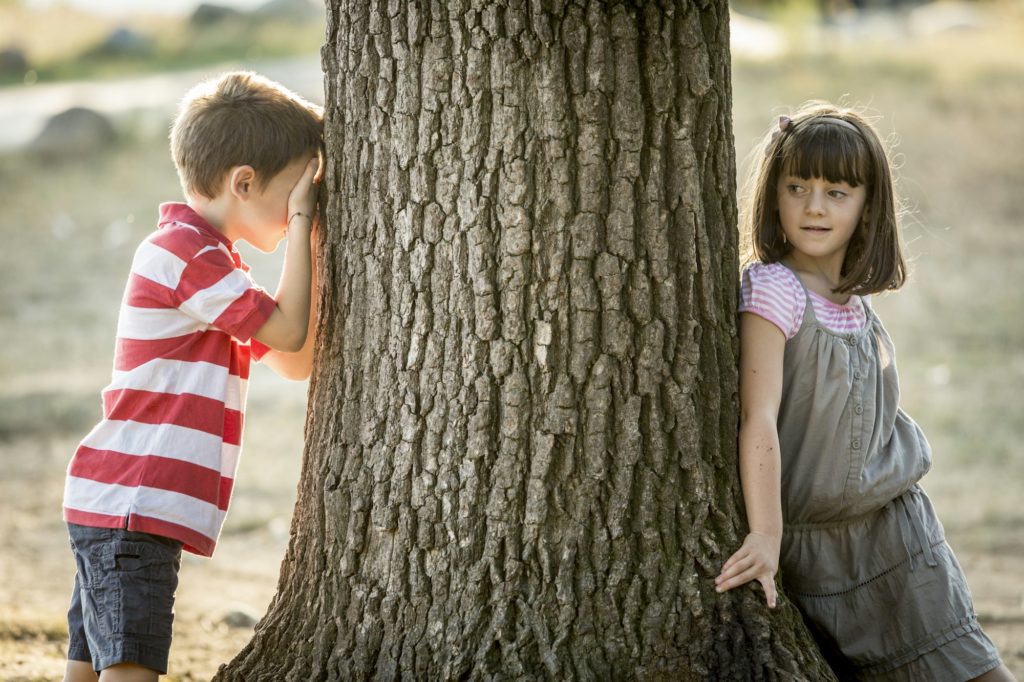 Little boy and girl playing hide and seek in nature