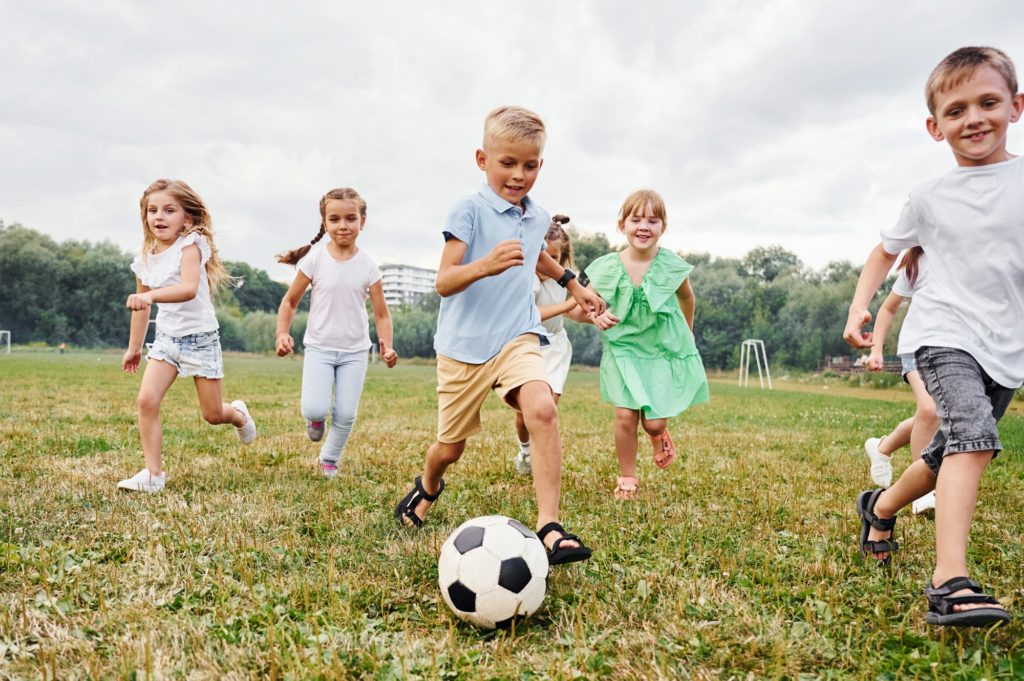 Soccer ball, playing together. Kids are having fun on the field at daytime